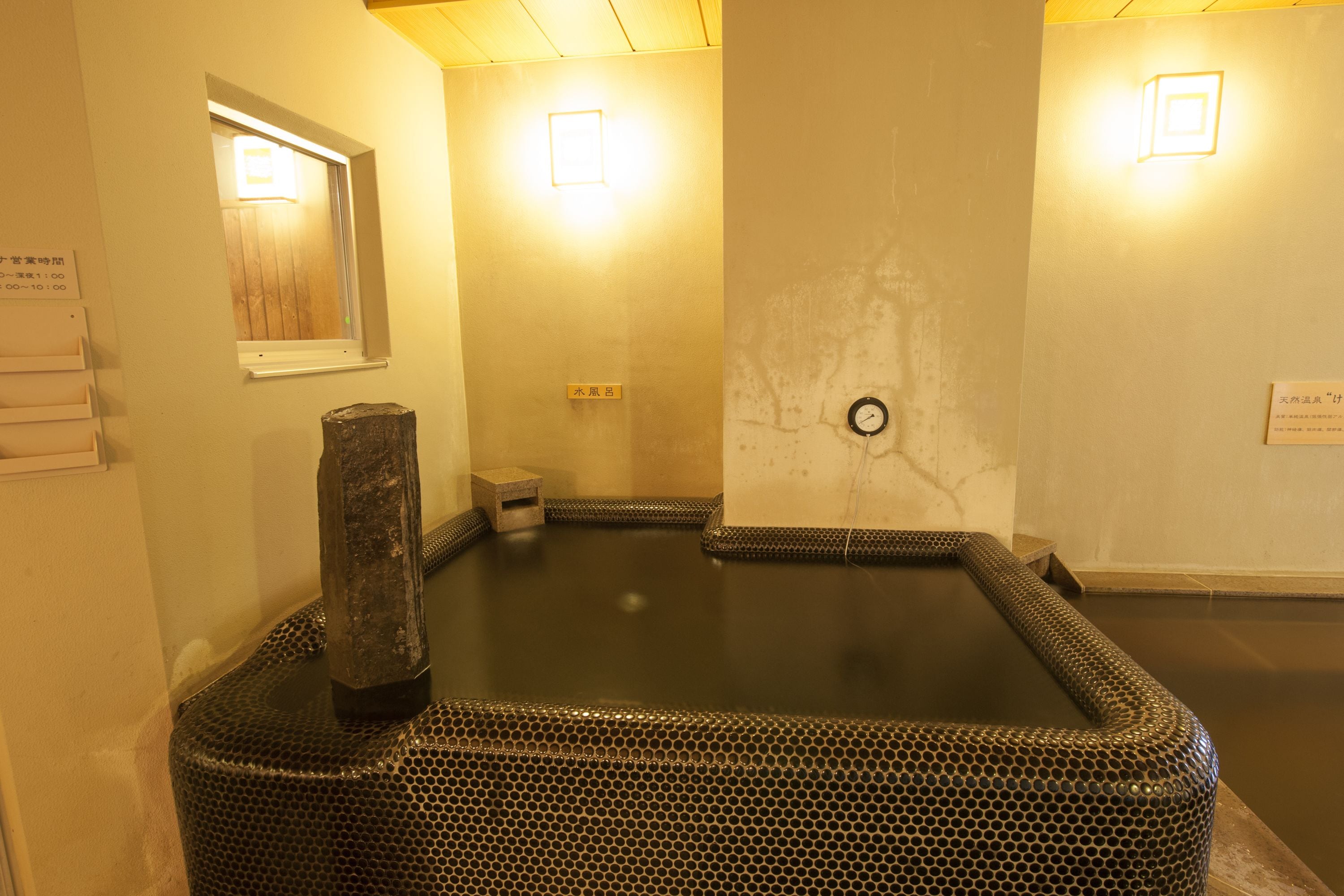 Un área de baños termales con una estructura de madera en el centro, rodeada por un piso de baldosas.