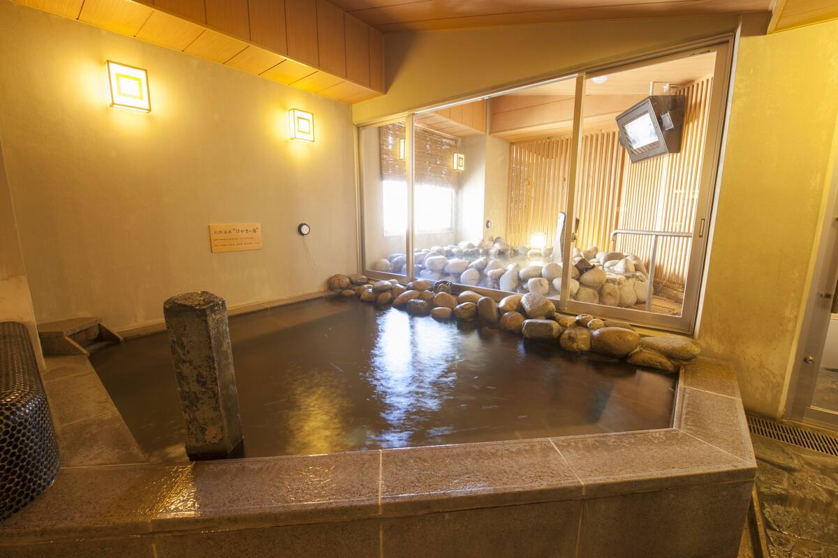Uma onsen japonesa tradicional com um banho de pedra rodeado por rochas e um banco de madeira.