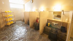 A public restroom with stone flooring, yellow storage bins, and individual cubicles with sinks and mirrors. - Dormy Inn Tsu Natural Hot Spring (Tsu)