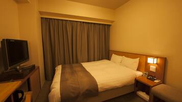 A hotel room with a bed, a television, a bedside table with a lamp, and a window with curtains.