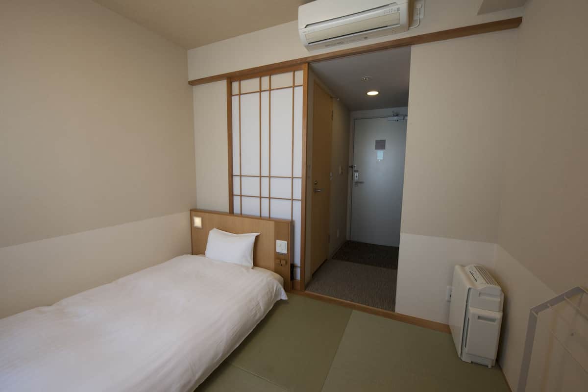 Quarto de hotel com uma cama, porta de correr estilo shoji, ar condicionado e radiador.