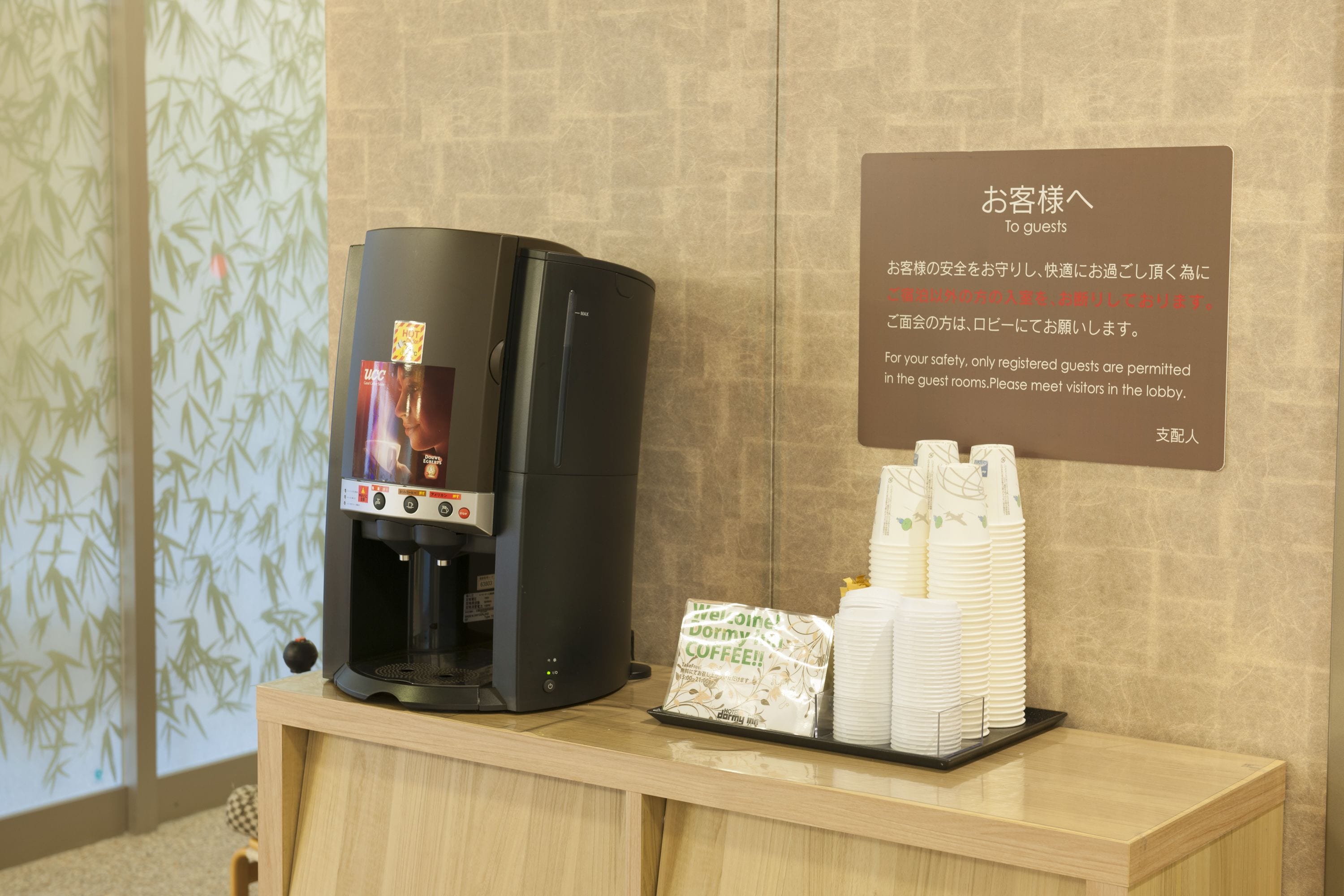 Eine Kaffeemaschine mit digitalem Display, ein Stapel Einwegbecher und ein Schild mit japanischem Text.