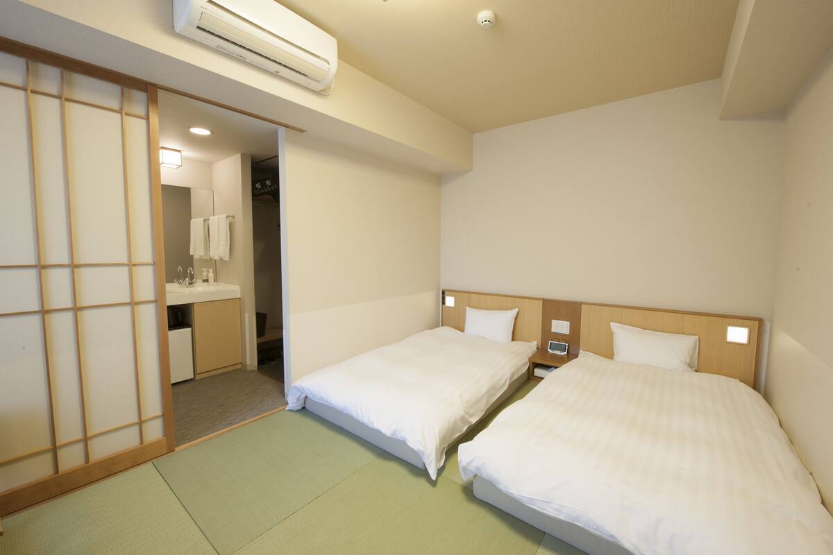 Quarto de hotel com duas camas, banheiro e um biombô shoji.