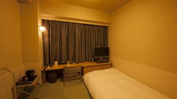 A hotel room with a bed, desk, chair, TV, and a small table with a kettle and cups.