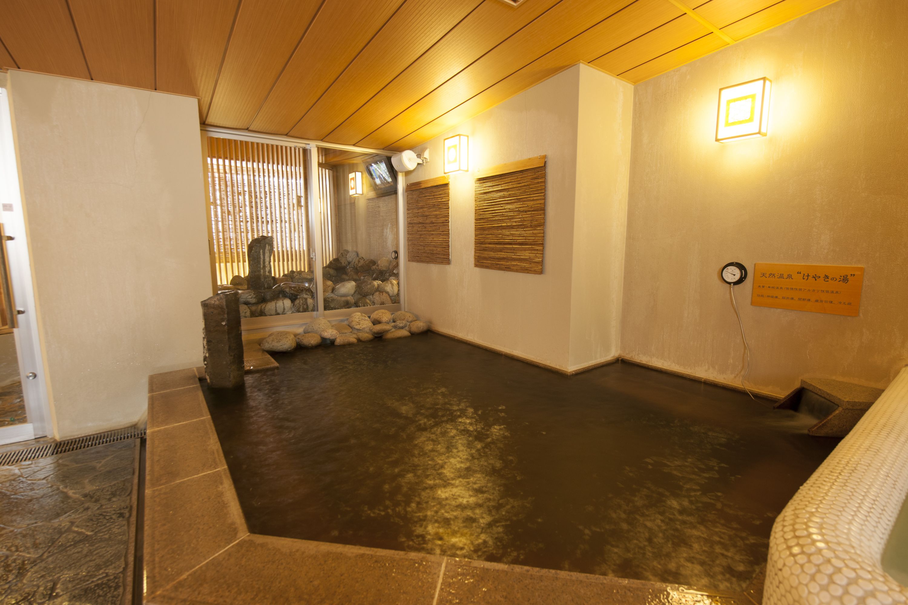 Un onsen japonais traditionnel, doté d’une baignoire en pierre, d’un plafond en bois et offrant une vue sur une zone boisée.