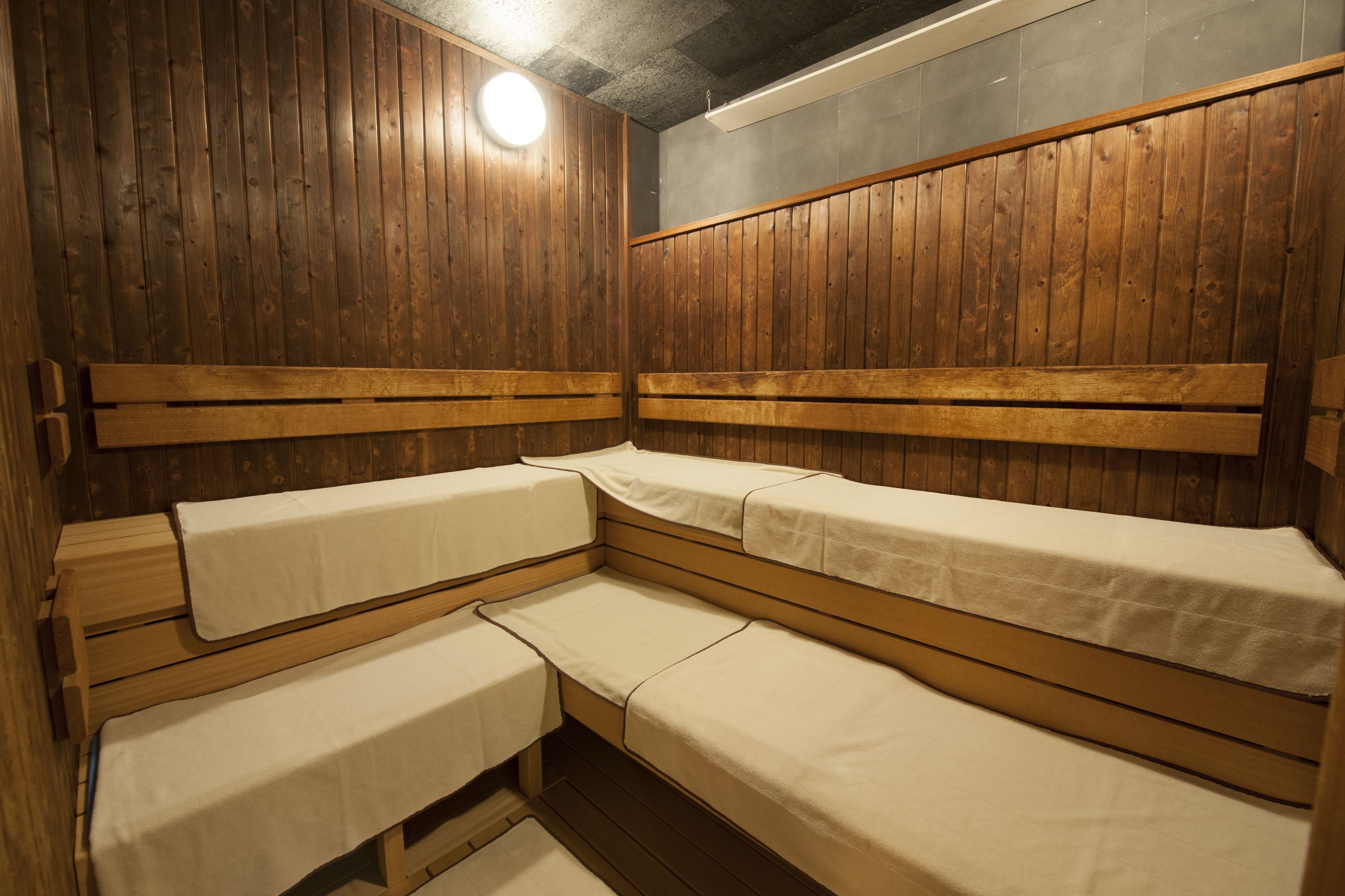 A sauna room with wooden benches and benches, a ceiling light, and a wooden wall.