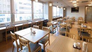A spacious restaurant with multiple dining tables and chairs, large windows providing natural light, and a flat-screen TV mounted on the wall. - Dormy Inn Tsu Natural Hot Spring (Tsu)