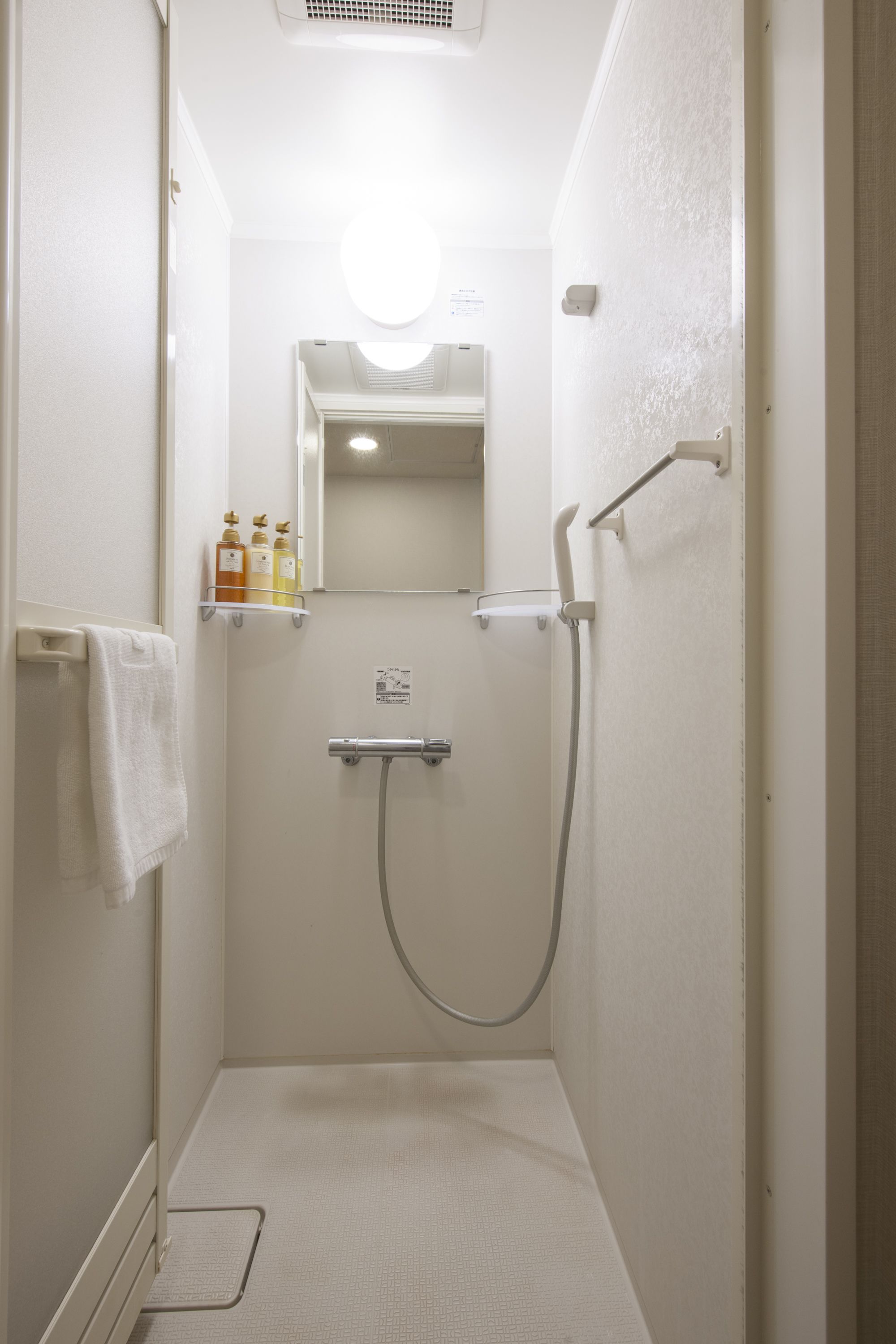 Un baño pequeño y estrecho con ducha, un perchero y un estante con artículos de aseo.