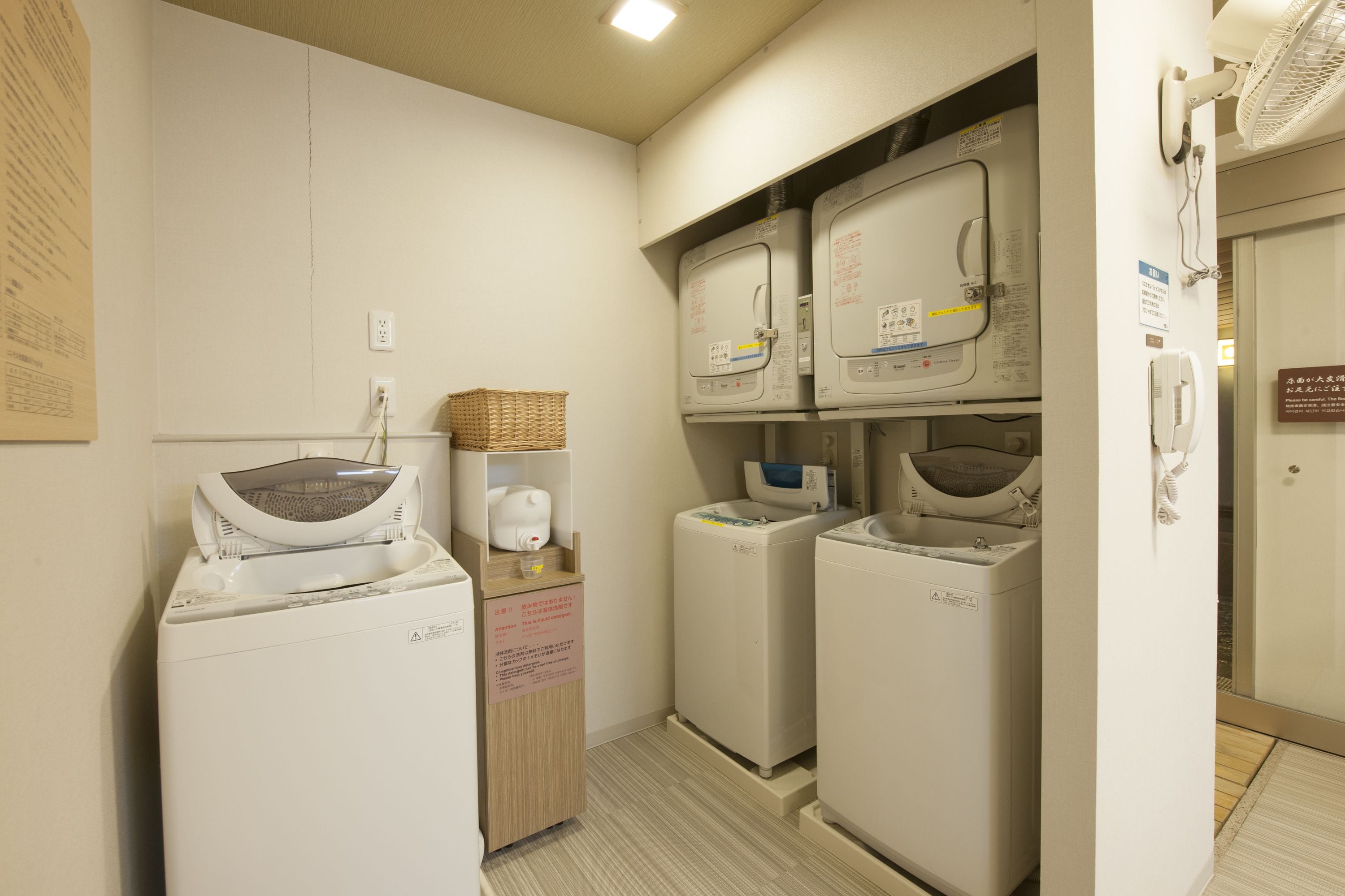 A laundry room with two stacked washers and dryers, a basket on the dryer, and a sign with instructions.