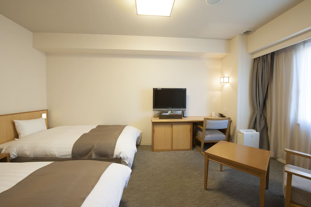 Quarto de hotel com duas camas, uma escrivaninha, uma televisão e uma cadeira.