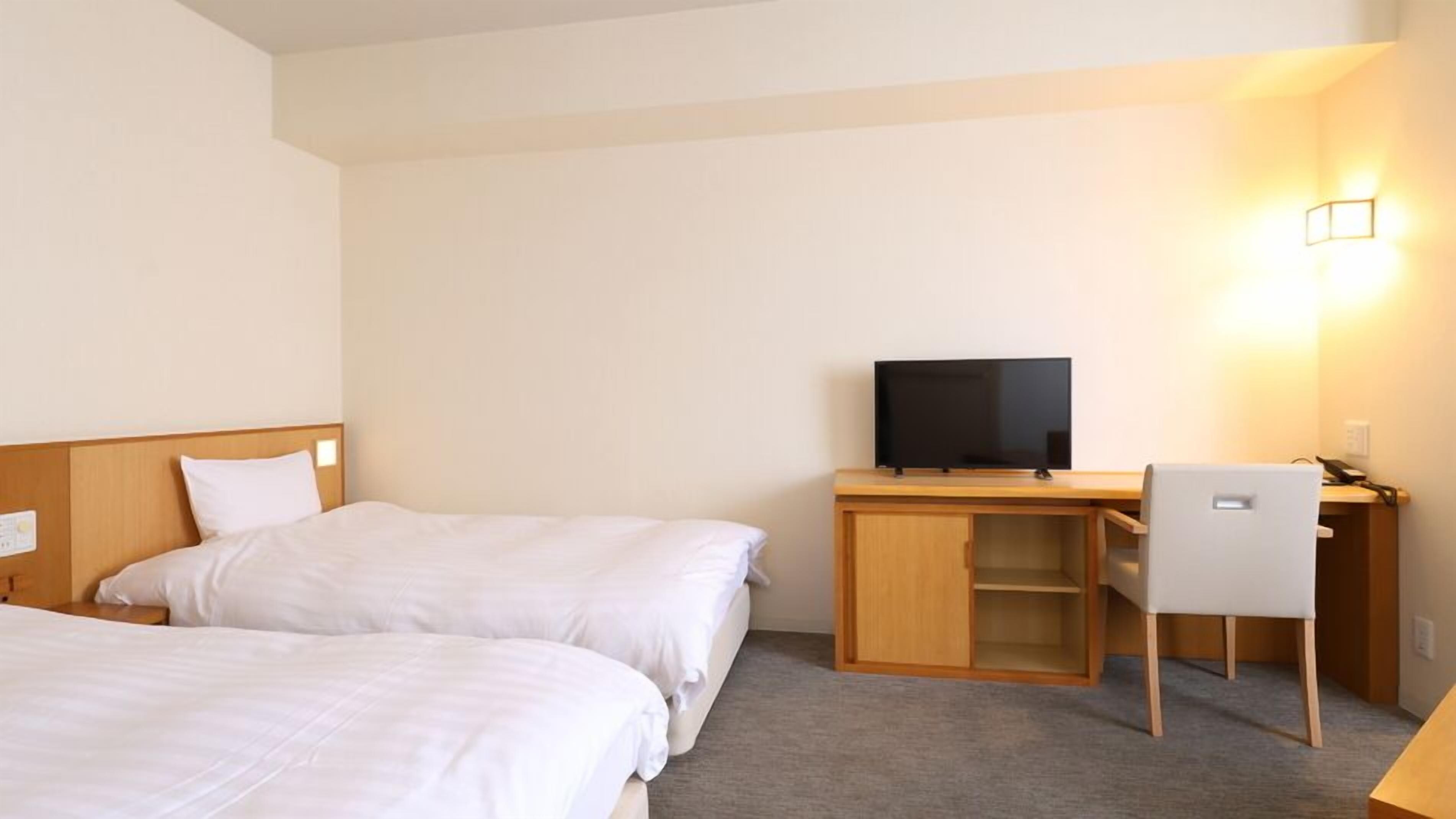 A hotel room with two beds, a desk, a chair, a television, and a wall-mounted light.