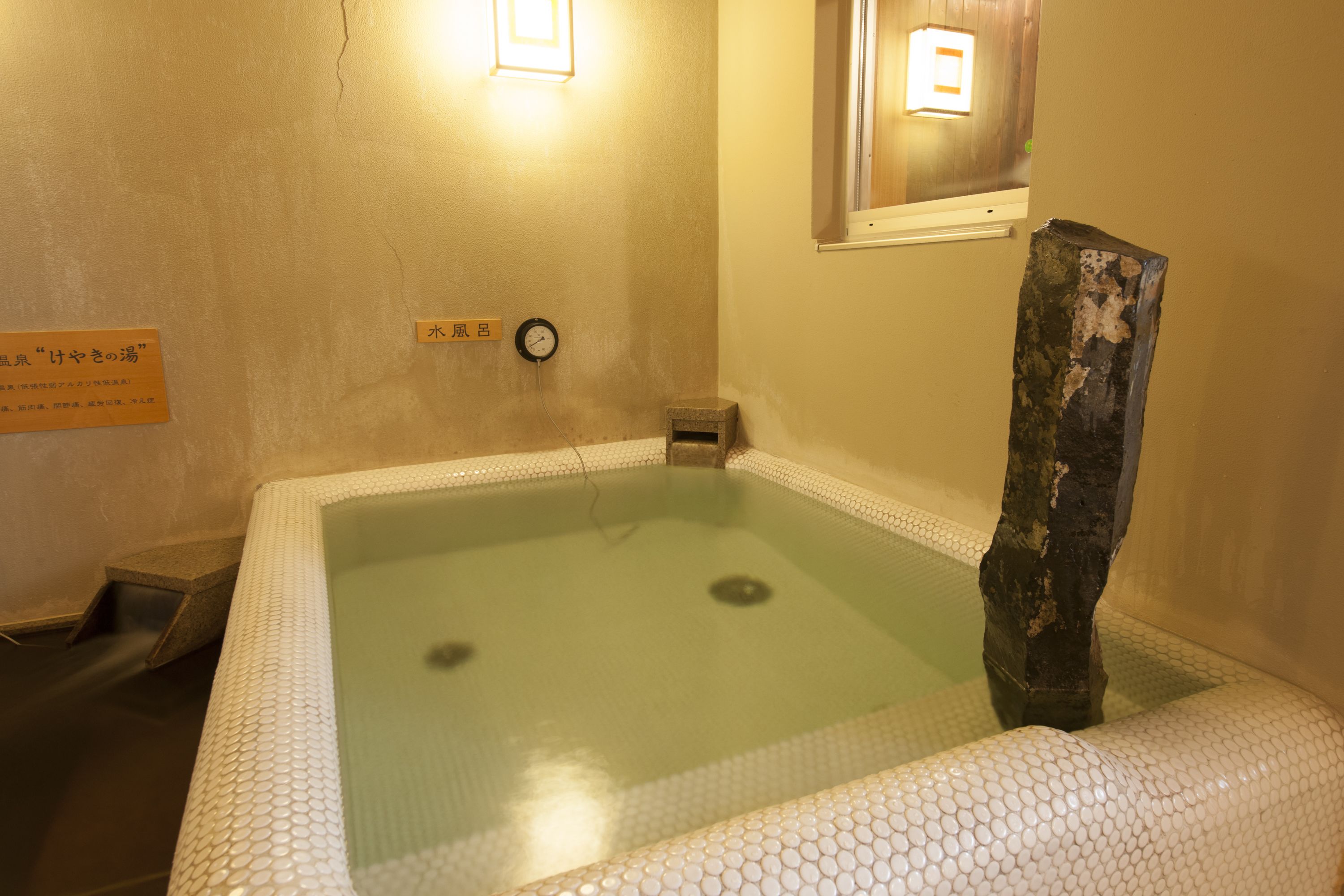 A traditional Japanese onsen with a wooden structure in the center, a small stone bench, and a wall-mounted clock.