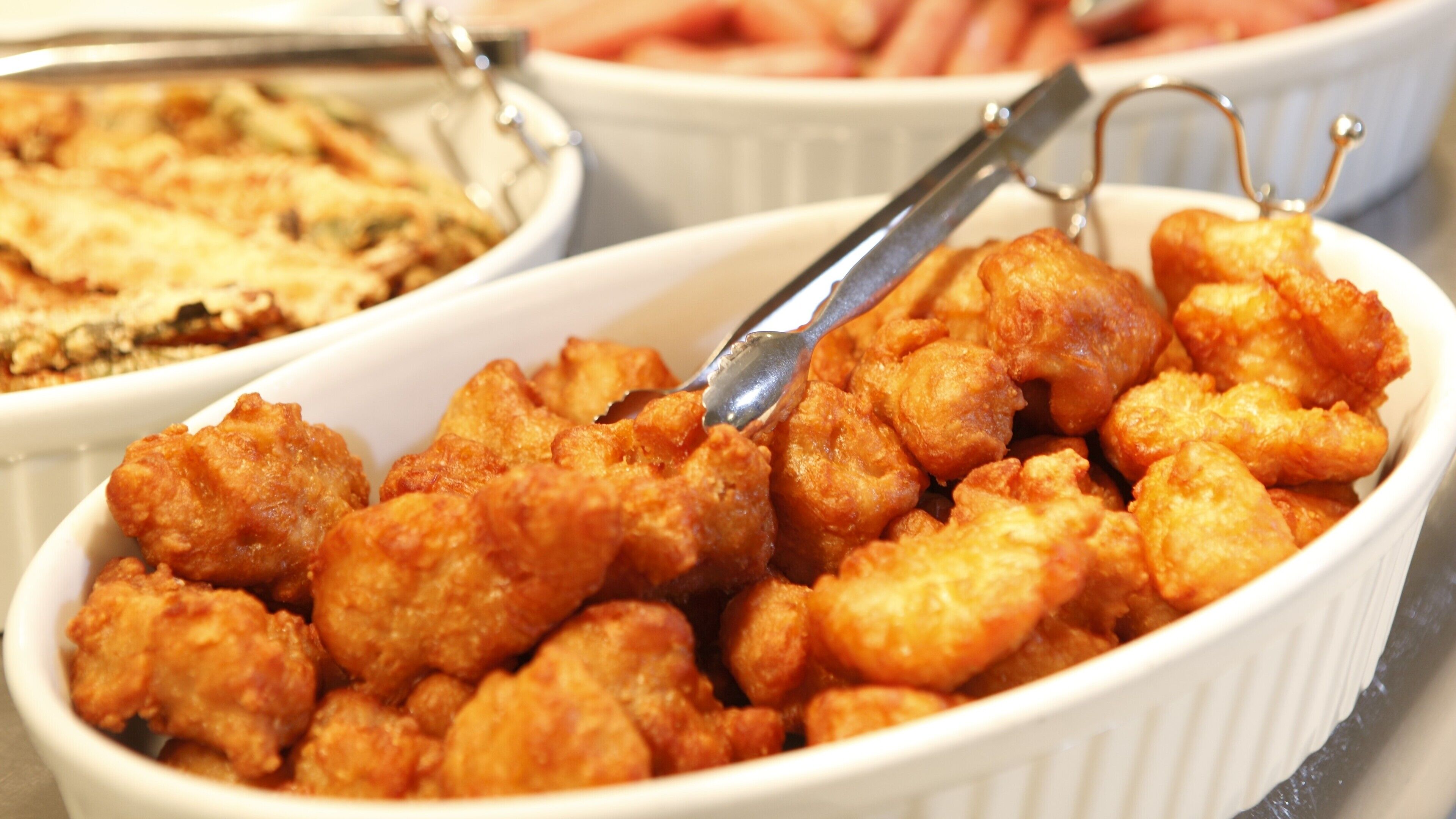 A white ceramic dish filled with fried chicken pieces, accompanied by a serving spoon.