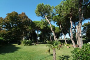 A well-maintained garden with various trees, a lawn, and a bench. - Punta Nord Village & Hotel (Rimini)
