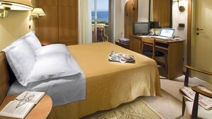 A hotel room with a bed, a desk with a laptop, a television, and a view of the sea through a sliding door. - Punta Nord Village & Hotel (Rimini)