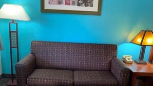 Una habitación con pared azul, sofá estampado, mesa de centro de madera, lámpara de pie y un cuadro enmarcado en la pared.