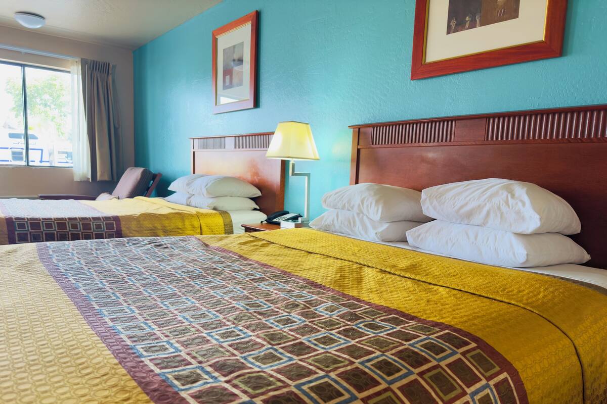 Habitación de hotel con dos camas, cada una con una colcha estampada y almohadas blancas. Se observa un cabecero de madera, una lámpara de noche y un cuadro enmarcado en la pared.