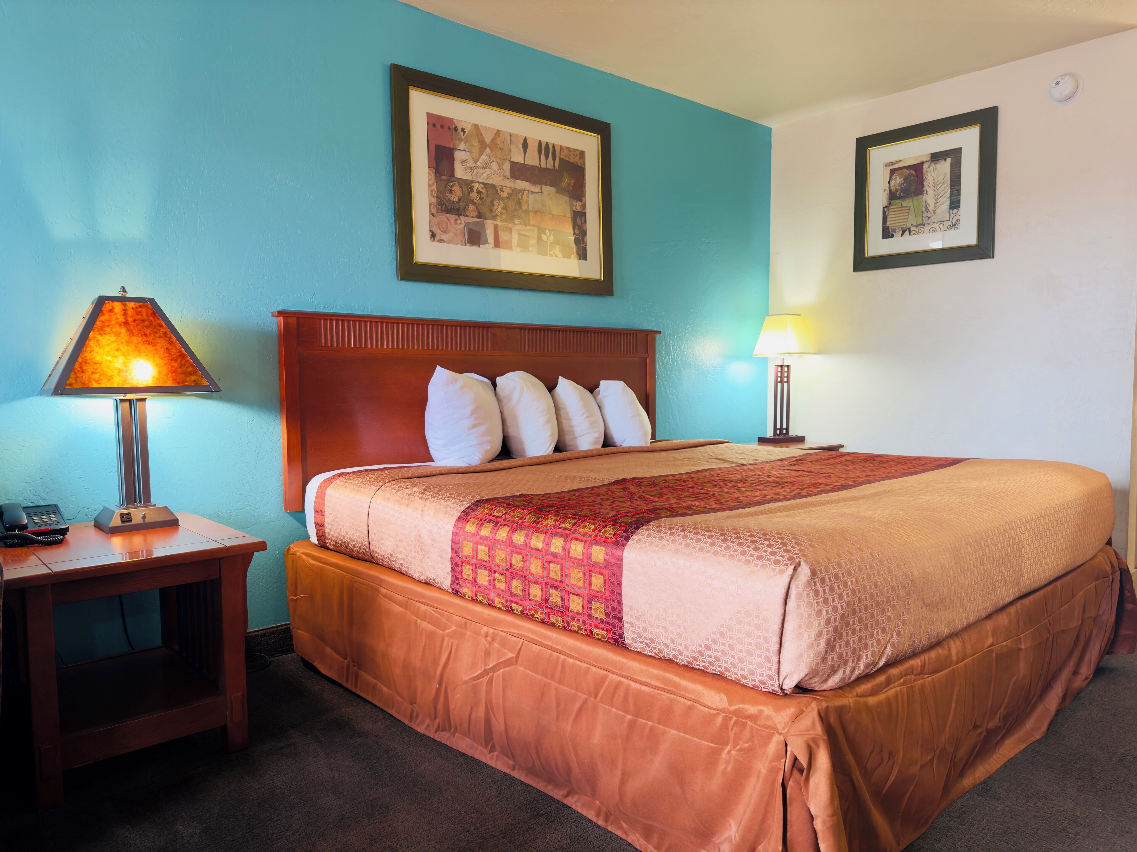 Una habitación de hotel con cama, dos lámparas de noche, un teléfono y dos cuadros en las paredes.