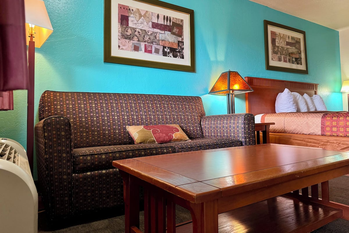 Una habitación con un sofá estampado, una mesa de madera y dos cuadros en paredes color turquesa.