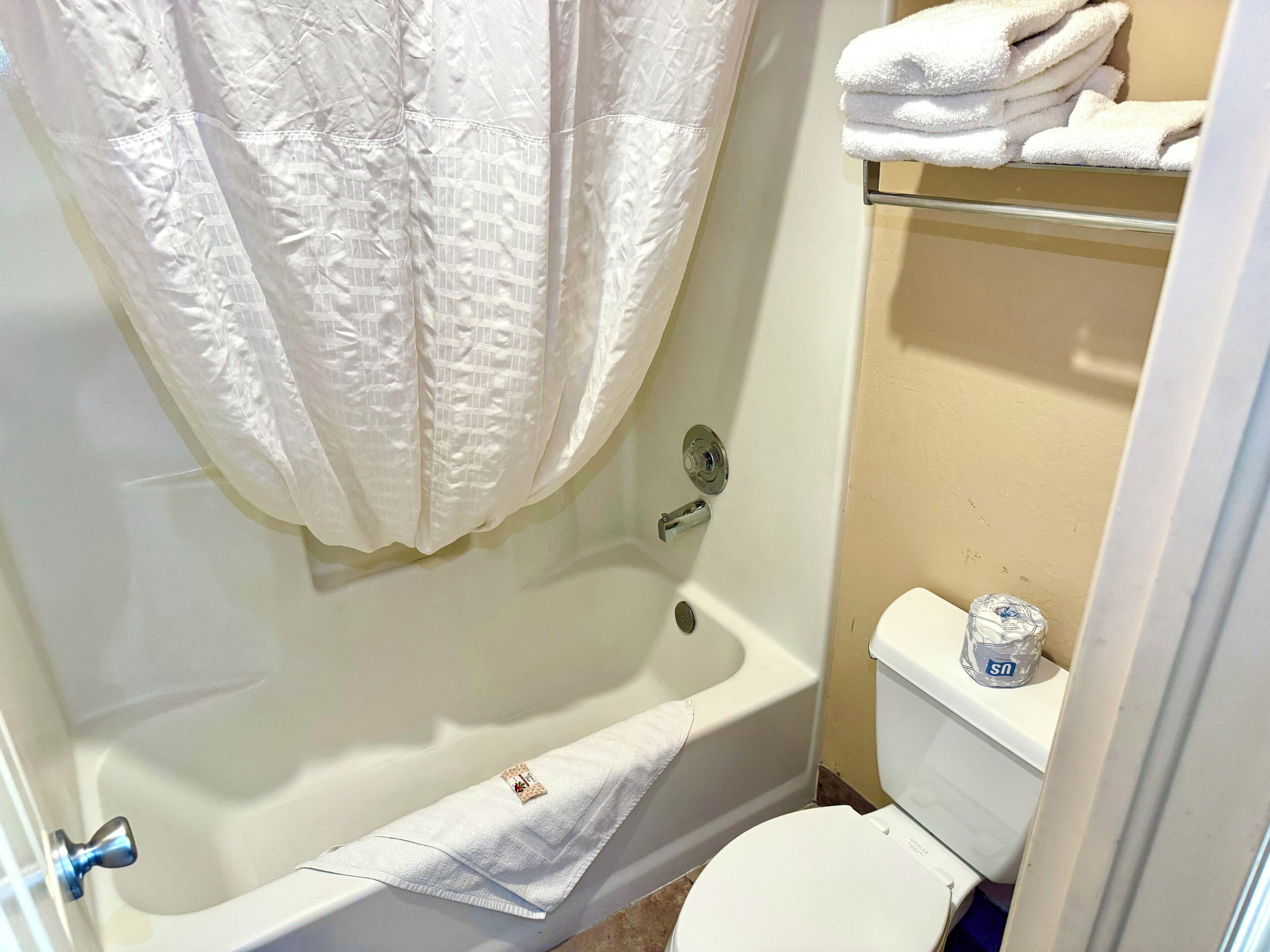 A bathroom with a bathtub, toilet, and a towel rack with folded towels.