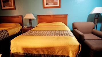 Habitación de hotel con dos camas, una silla y una mesita de noche con lámpara.