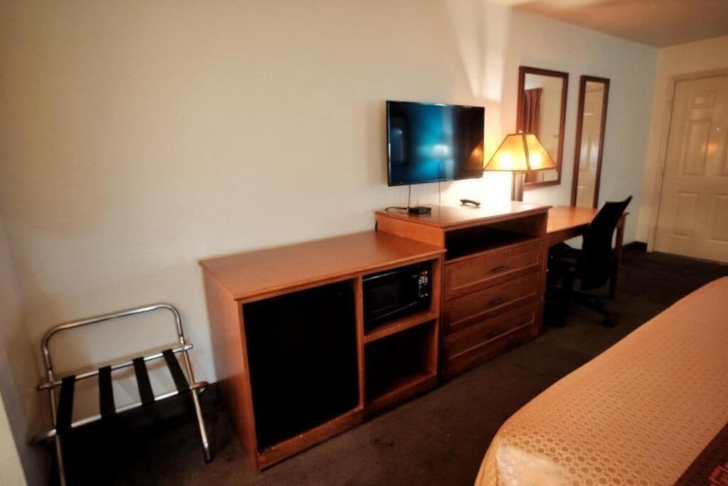 A hotel room with a bed, a desk with a television, a lamp, a chair, and a wardrobe.