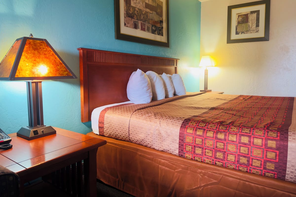 Una cama bien hecha con un edredón estampado, un cabecero de madera y dos lámparas de noche.