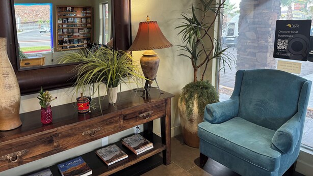 Una habitación acogedora con una consola de madera, un sillón azul, un espejo grande y vistas a la calle.