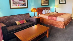 Una habitación de hotel con un sofá, una cama, una mesa de madera y dos cuadros en las paredes.
