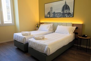 Habitación de hotel con dos camas, una mesita de noche con teléfono y un cuadro en la pared que representa un paisaje urbano.