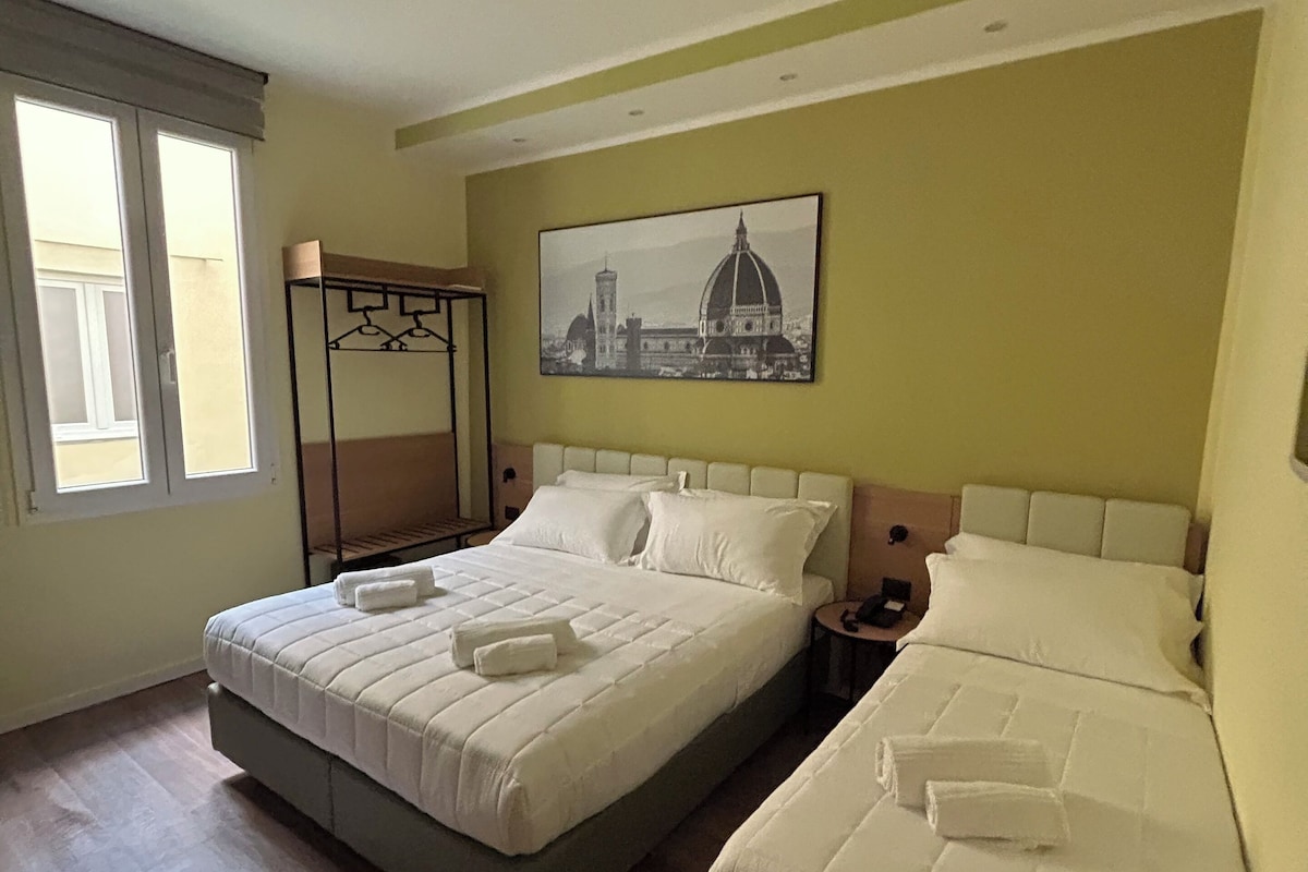 A hotel room with two beds, a painting of a cityscape, and a window with curtains.