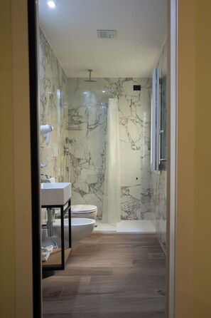 Un baño moderno con ducha de mármol, lavamanos e inodoro.