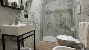 A modern bathroom with a marble wall, a glass-enclosed shower, a white sink, and a toilet. - JR Hotels Hermes Firenze (Florence)