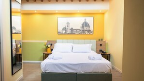 A hotel room with a bed, a nightstand, a mirror, and a cityscape painting on the wall. - JR Hotels Hermes Firenze (Florence)