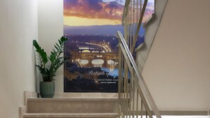 A staircase with beige steps and a metal railing, leading to a landing with a poster of a sunset cityscape. - JR Hotels Hermes Firenze (Florence)