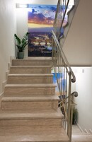 A staircase with beige steps and a metal railing, leading to a landing with a poster of a sunset cityscape.