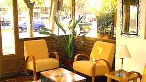 A cozy seating area with yellow chairs and a small table, a potted plant, and a window with a view of the street.