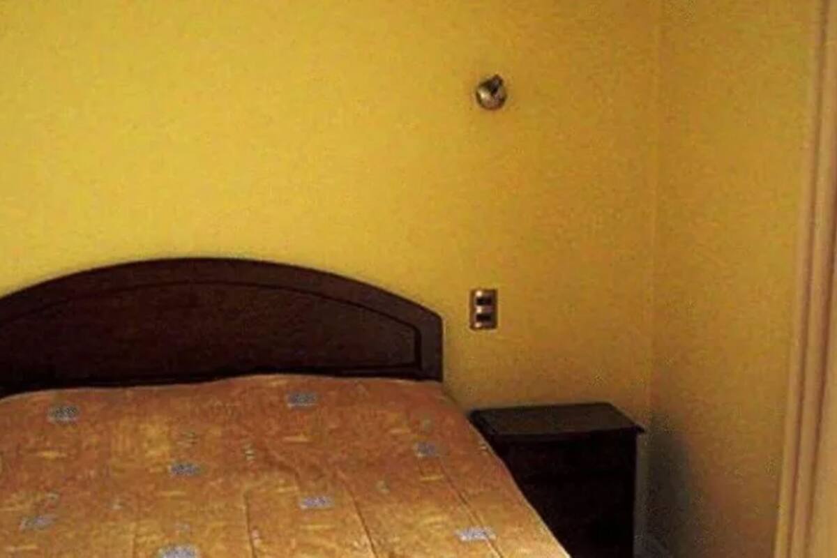 Una habitación con una cama de madera, una mesita de noche pequeña y un interruptor de luz en la pared.