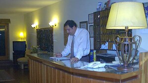A reception desk with a man working at it, a lamp, and a framed picture on the wall.
