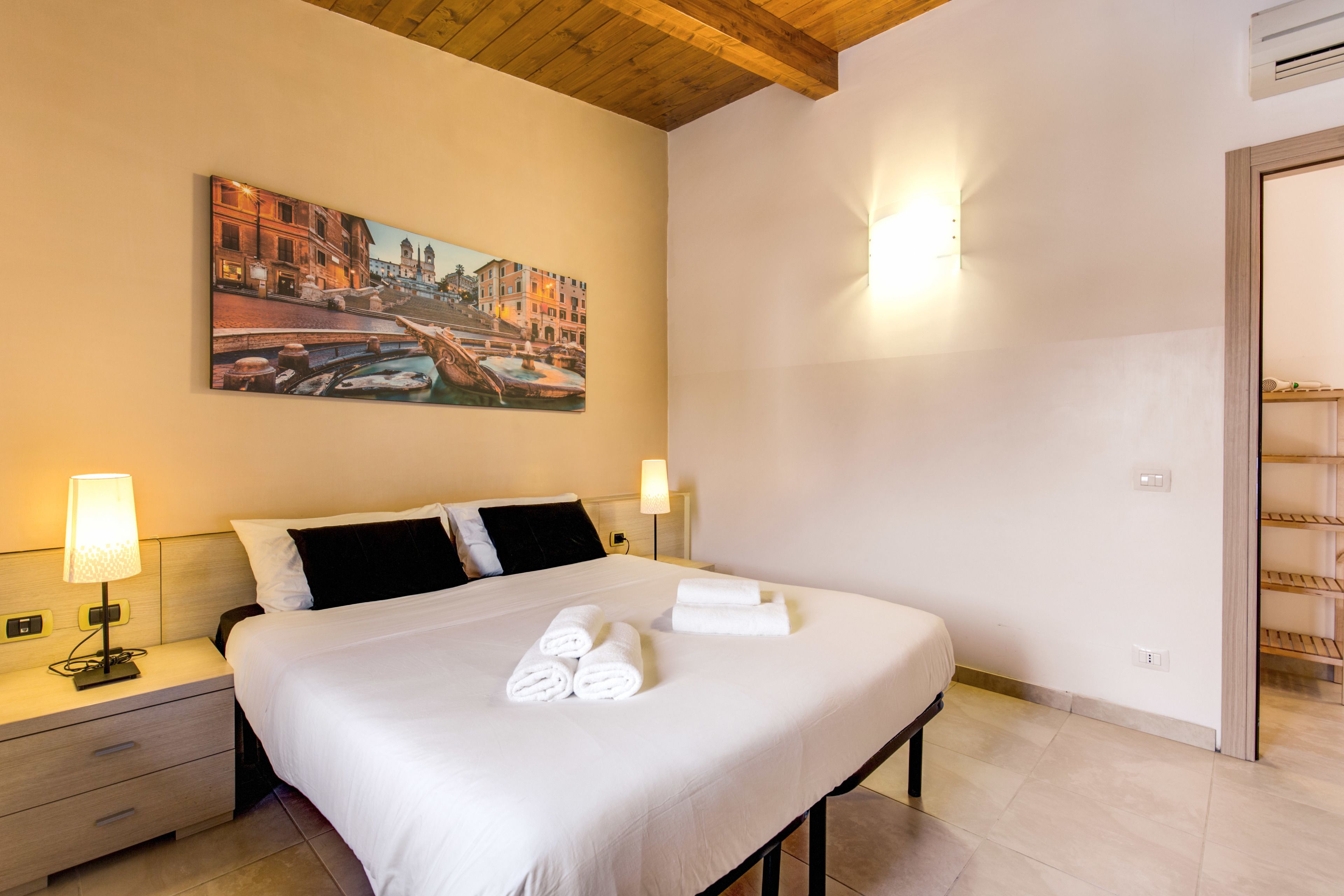 Habitación de hotel con una cama grande, dos mesitas de noche con lámparas, un cuadro en la pared y techo de madera.