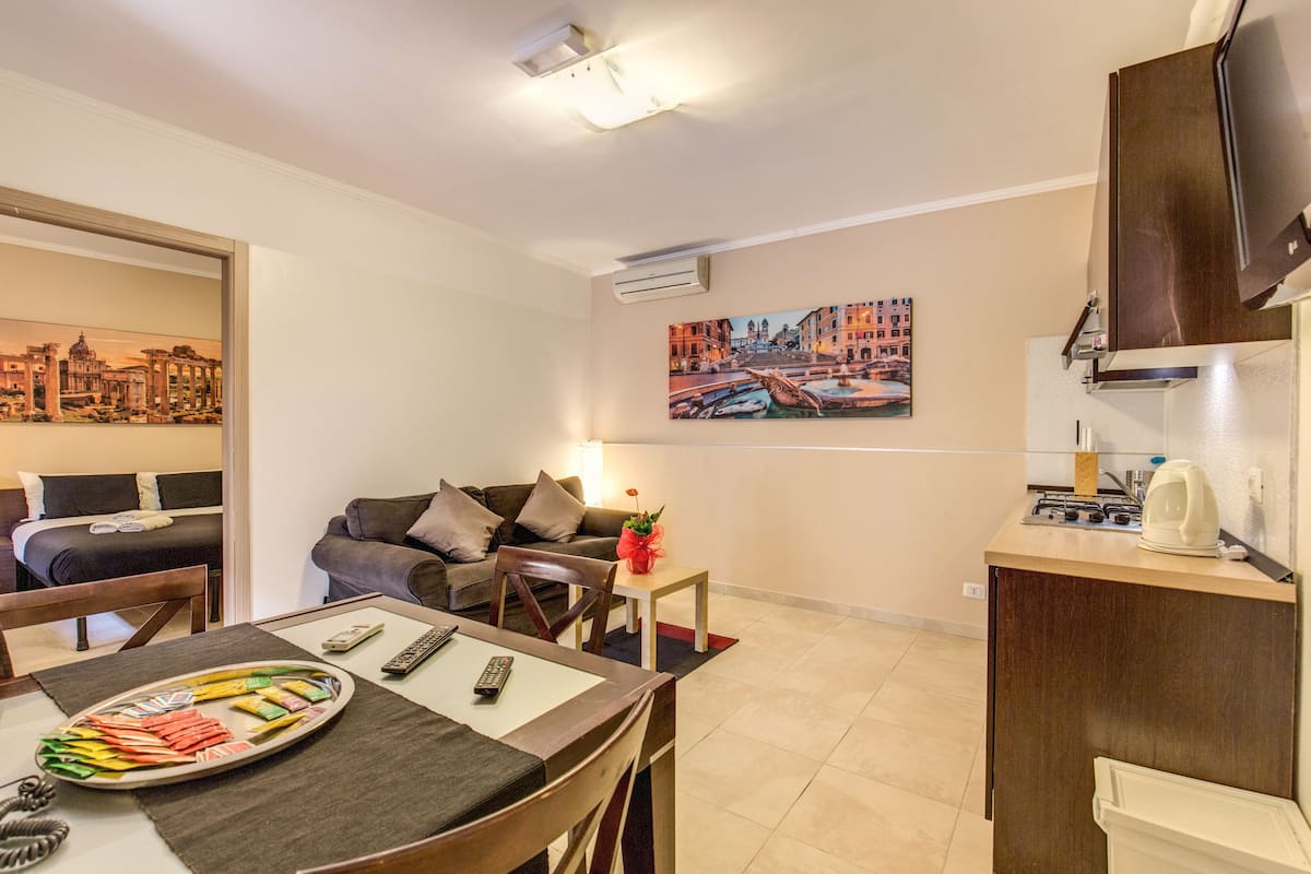A compact hotel room with a dining area, a kitchenette, a sofa, and a bed.