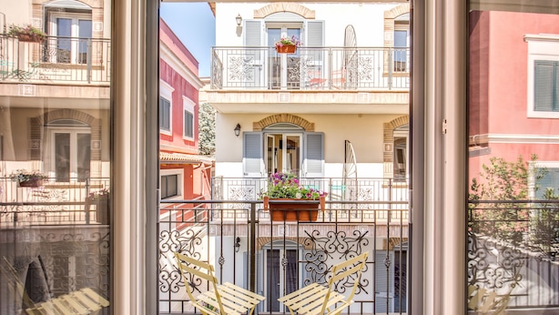 A balcony with two chairs, a potted plant, and a view of neighboring buildings. - Aurelia Vatican Apartments (Rome)