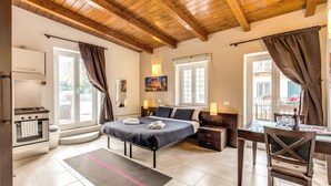 A bedroom with a bed, bedside tables, a desk with a chair, a window, and a view of the outside. - Aurelia Vatican Apartments (Rome)