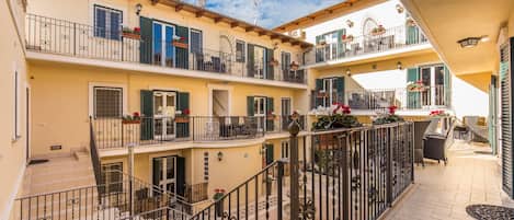Un immeuble à plusieurs étages doté de balcons, d’un espace extérieur aménagé pour s’asseoir et de plantes en pot.