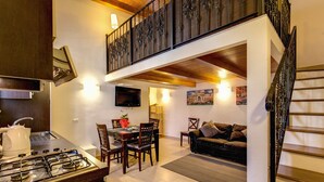 A modern kitchen with a gas stove, dining table, and chairs. There is a staircase leading to an upper level with a balcony. - Aurelia Vatican Apartments (Rome)