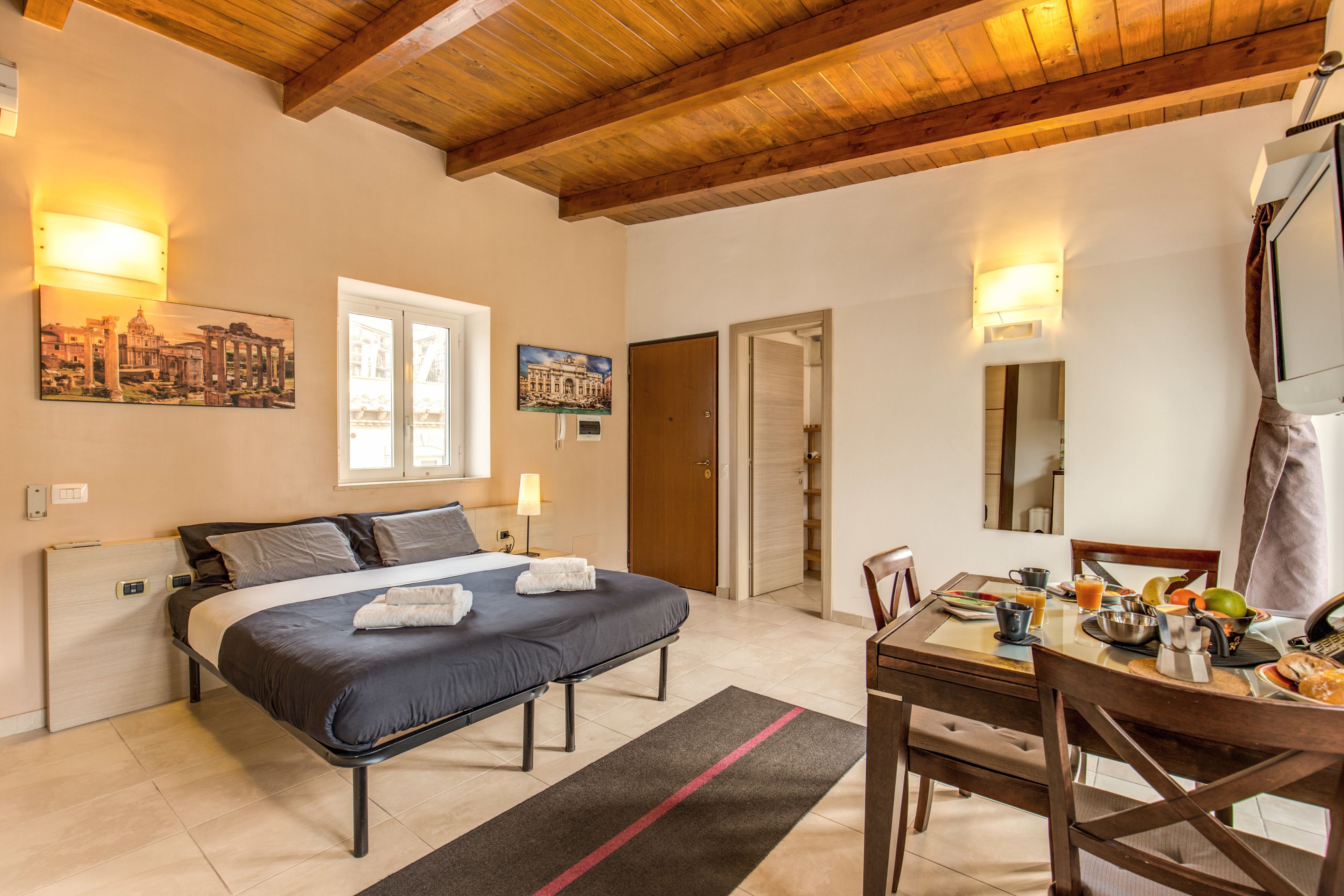 Une chambre à coucher avec un lit, un bureau et une chaise. Il y a deux tableaux au mur, une porte et une fenêtre.
