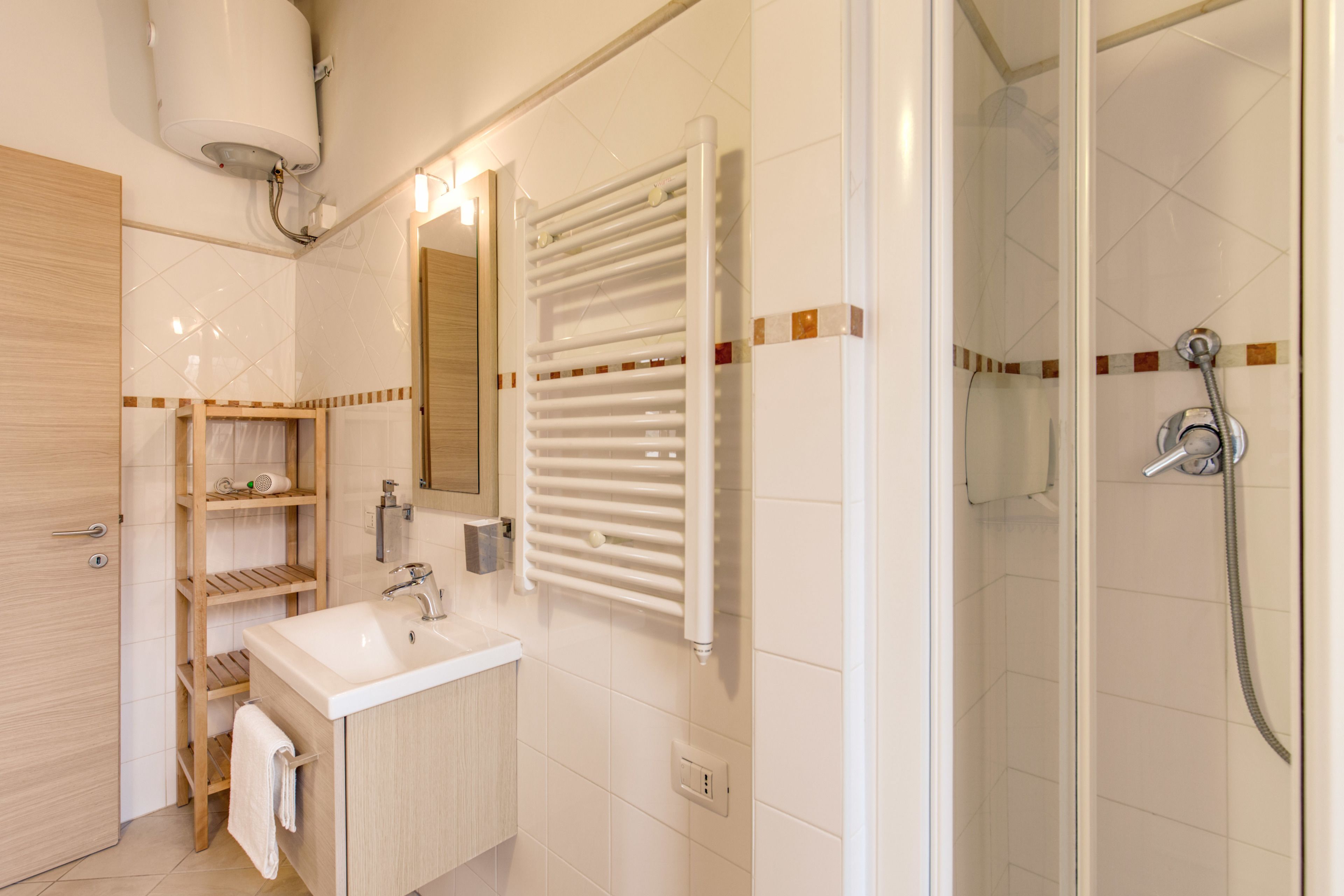 A modern bathroom with a sink, mirror, towel rack, shower, and a towel hanging on the door.