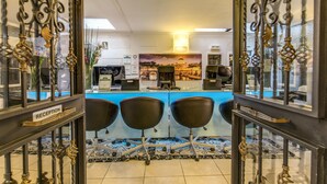 A reception area with a glass partition, three black chairs, a reception desk, and a wall-mounted sign. - Aurelia Vatican Apartments (Rome)