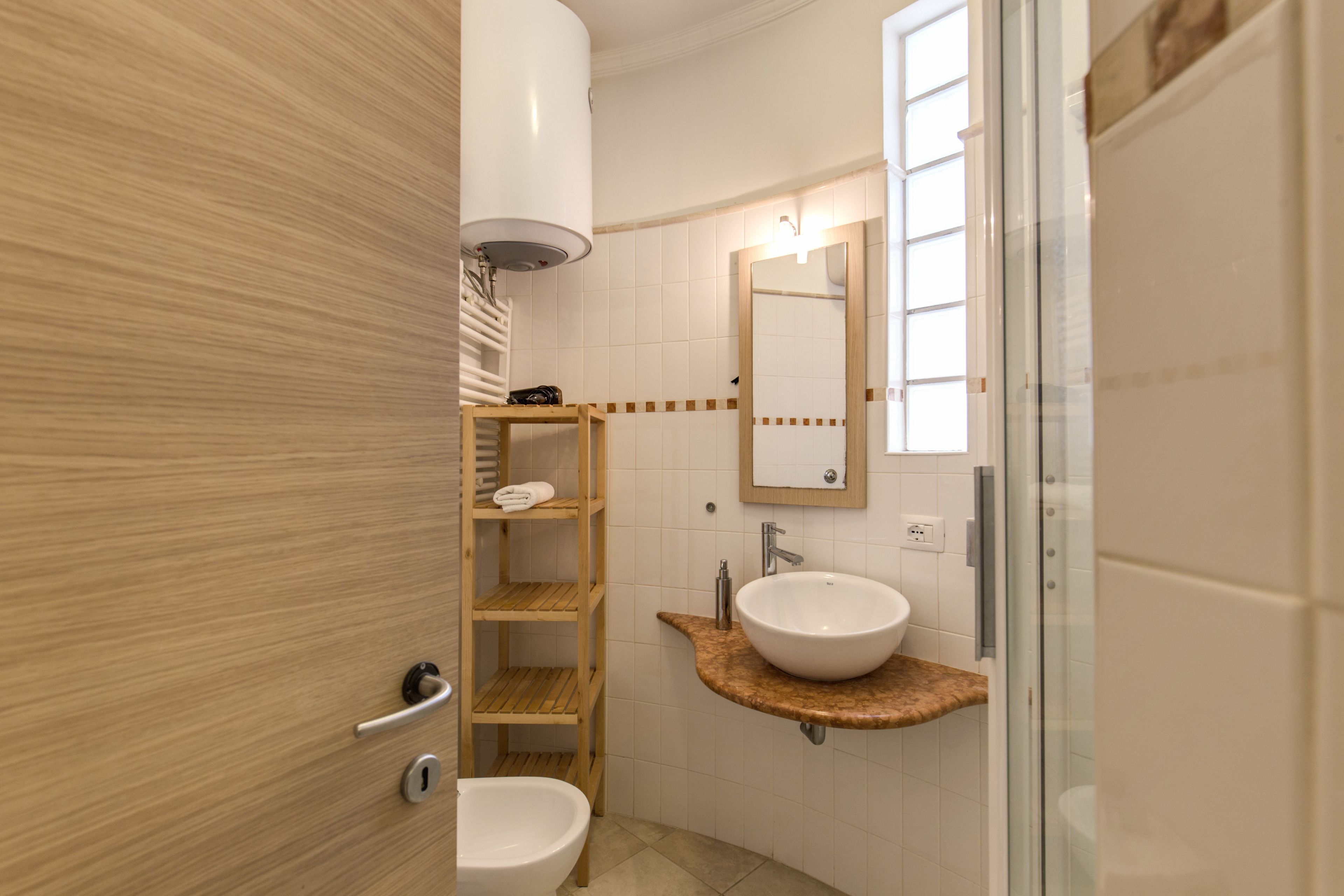 A modern bathroom with a wooden vanity, a white sink, a toilet, and a glass shower enclosure.