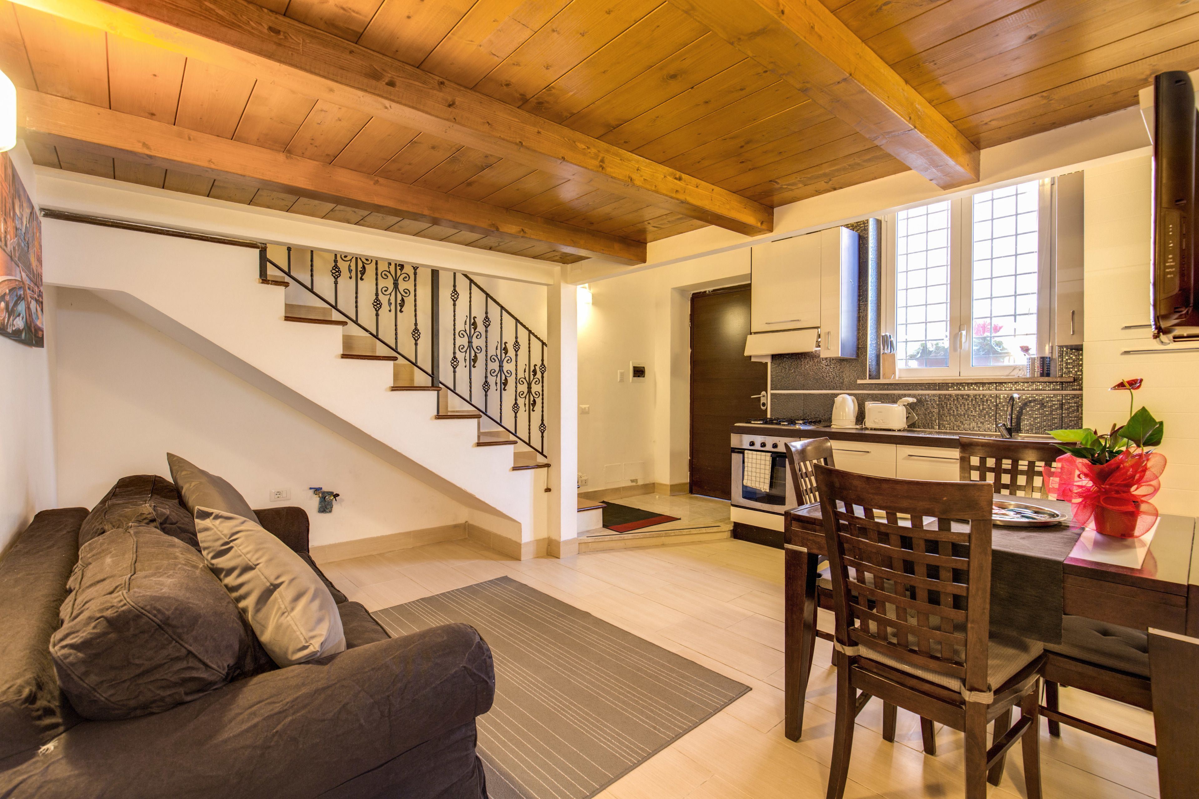 A modern kitchen with wooden beams, a dining area with a table and chairs, and a staircase leading to another level.